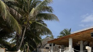 A beachside lounge area with striped lounge chairs, a thatched-roof structure, and palm trees. - Maria's Kan Kin with Private Beach (Isla Mujeres)