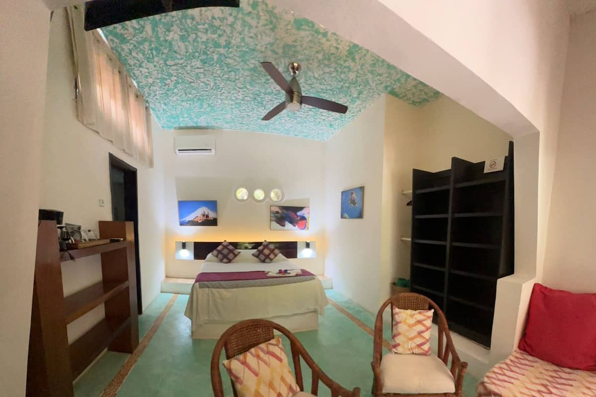 A bedroom with a bed, two chairs, a desk, and a ceiling fan.