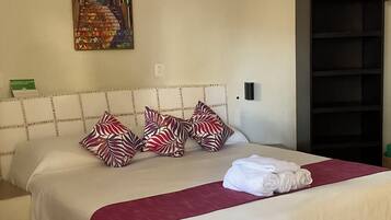 A hotel room with a bed, pillows, a painting, a ceiling fan, and a bookshelf.