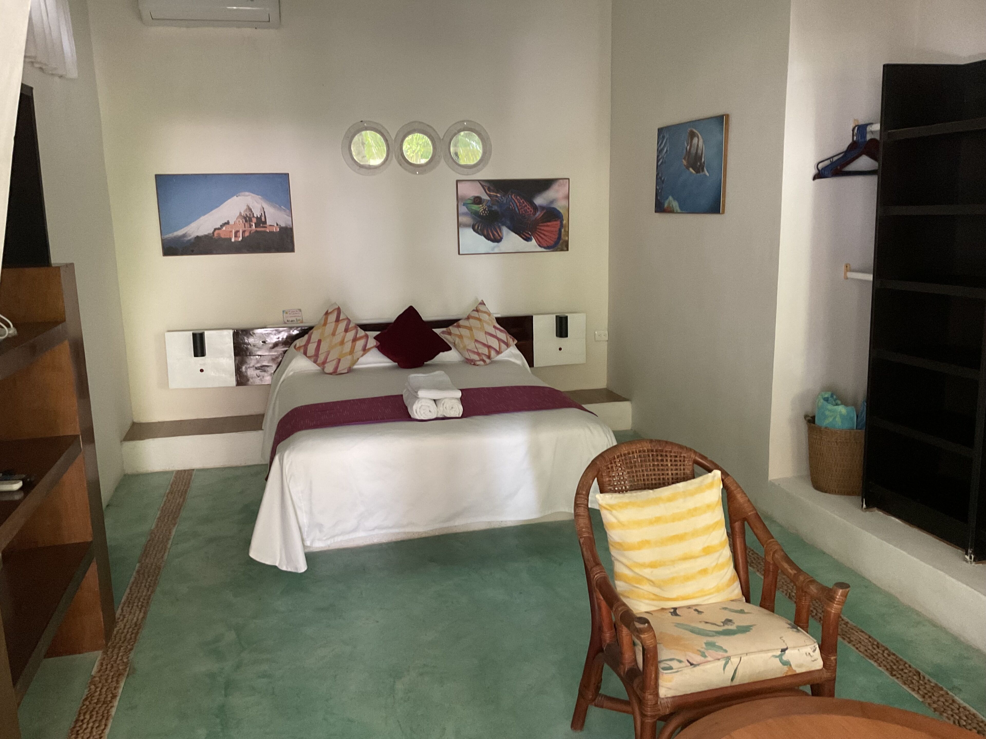 Una habitación de hotel con una cama, una silla, una estantería con objetos y decoración en la pared.