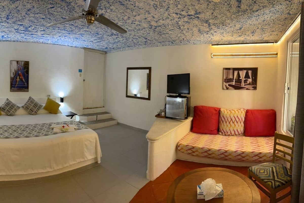 A hotel room with a bed, a sofa, a TV, and a ceiling fan.