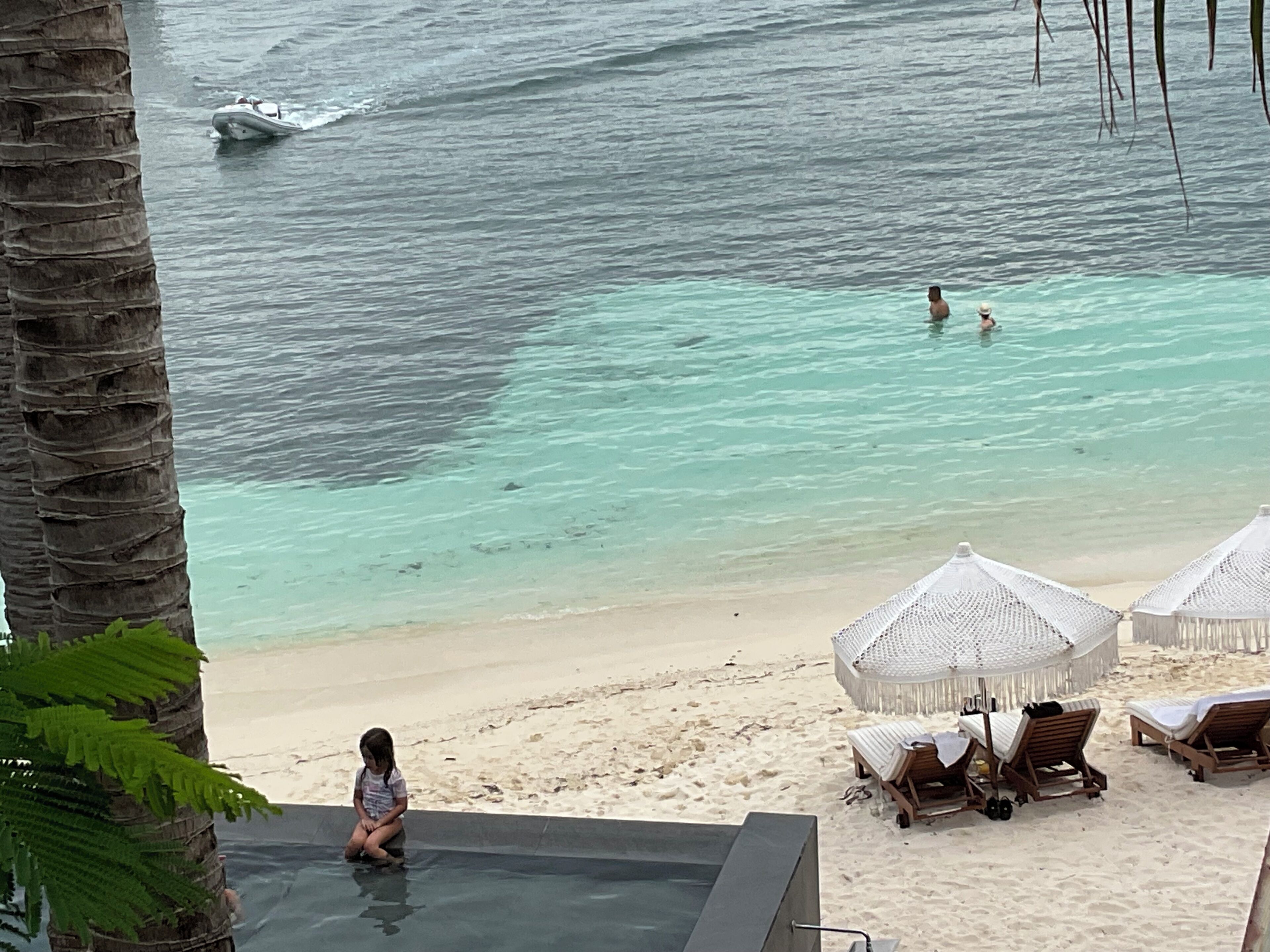 A beach with clear turquoise water, a child playing in the shallow water, and beach chairs and umbrellas.