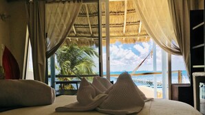 A hotel room with a bed, a view of the beach, and a thatched roof. - Maria's Kan Kin with Private Beach (Isla Mujeres)