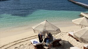 A beach with thatched umbrellas, lounge chairs, and a pier extending into the ocean. - Maria's Kan Kin with Private Beach (Isla Mujeres)