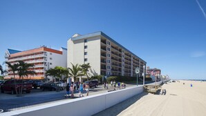 A beachfront hotel with multiple floors, a parking area, and a sandy beach in the background. - The Spinnaker Hotel (Ocean City)