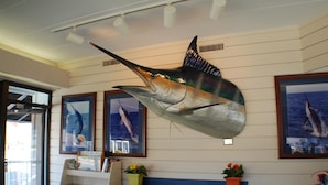 A room with a large fish mural on the wall, a wooden cabinet with drawers, and a window with a view of the ocean. - The Spinnaker Hotel (Ocean City)