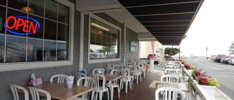 An outdoor seating area with tables and chairs, a 'OPEN' sign, and a view of parked cars and a street.