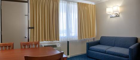Quarto de hotel com mesa de jantar, cadeiras, sofá e janela com cortinas.