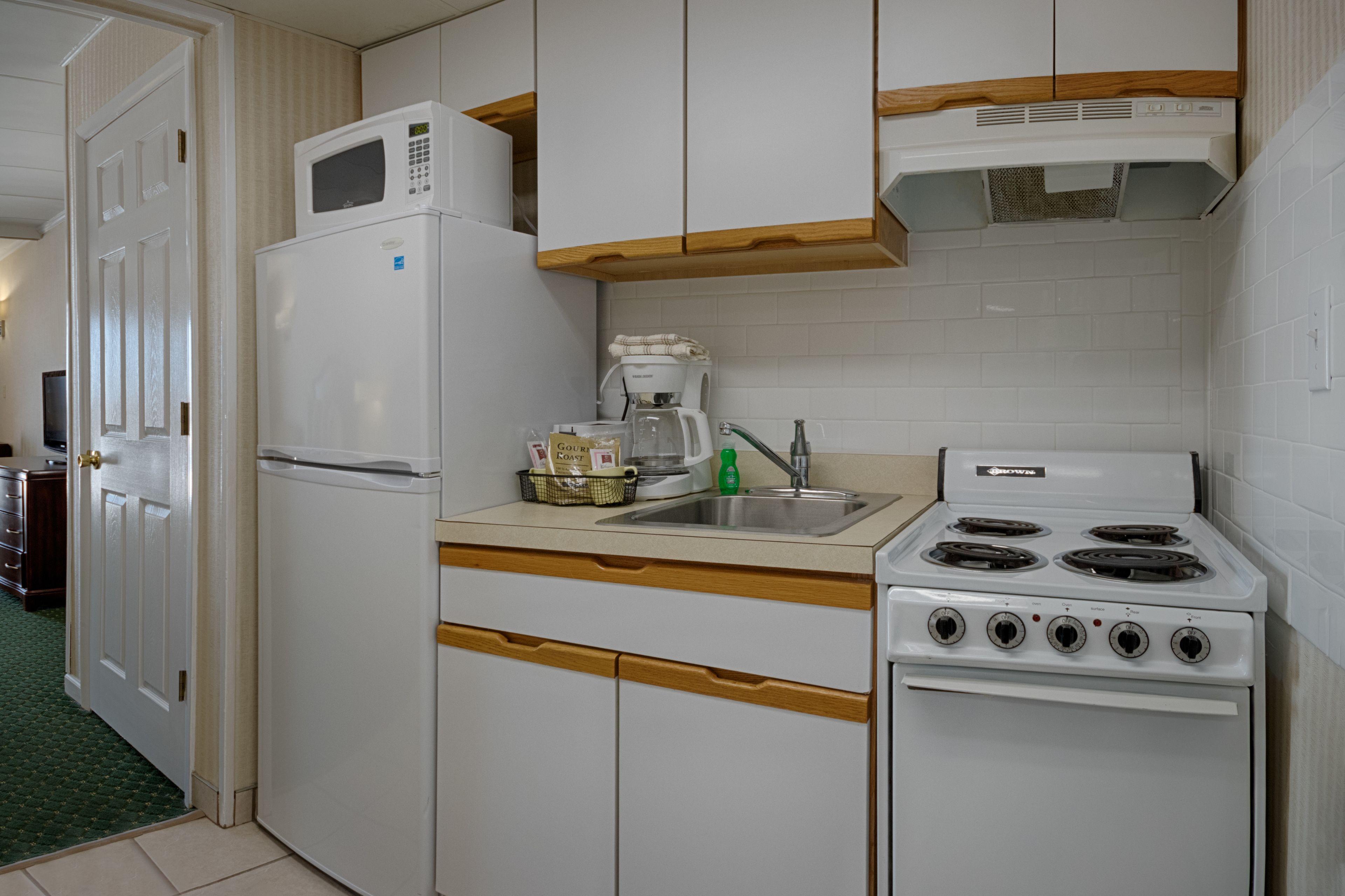 Cozinha compacta equipada com geladeira, micro-ondas, cafeteira, pia e fogão.