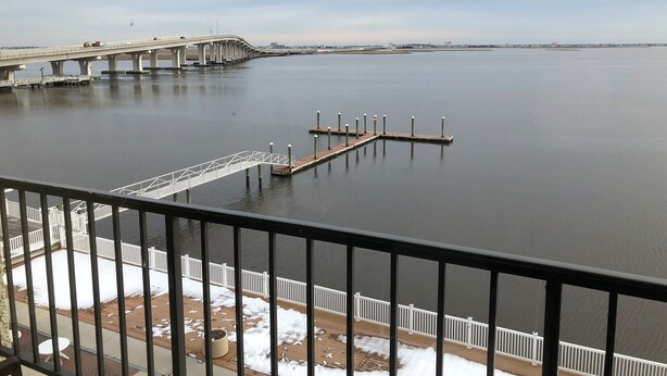 A view of a bridge over a calm body of water, a dock extending into the water, and a wooden deck with a railing in the foreground. - Pier 4 Hotel (Somers Point)