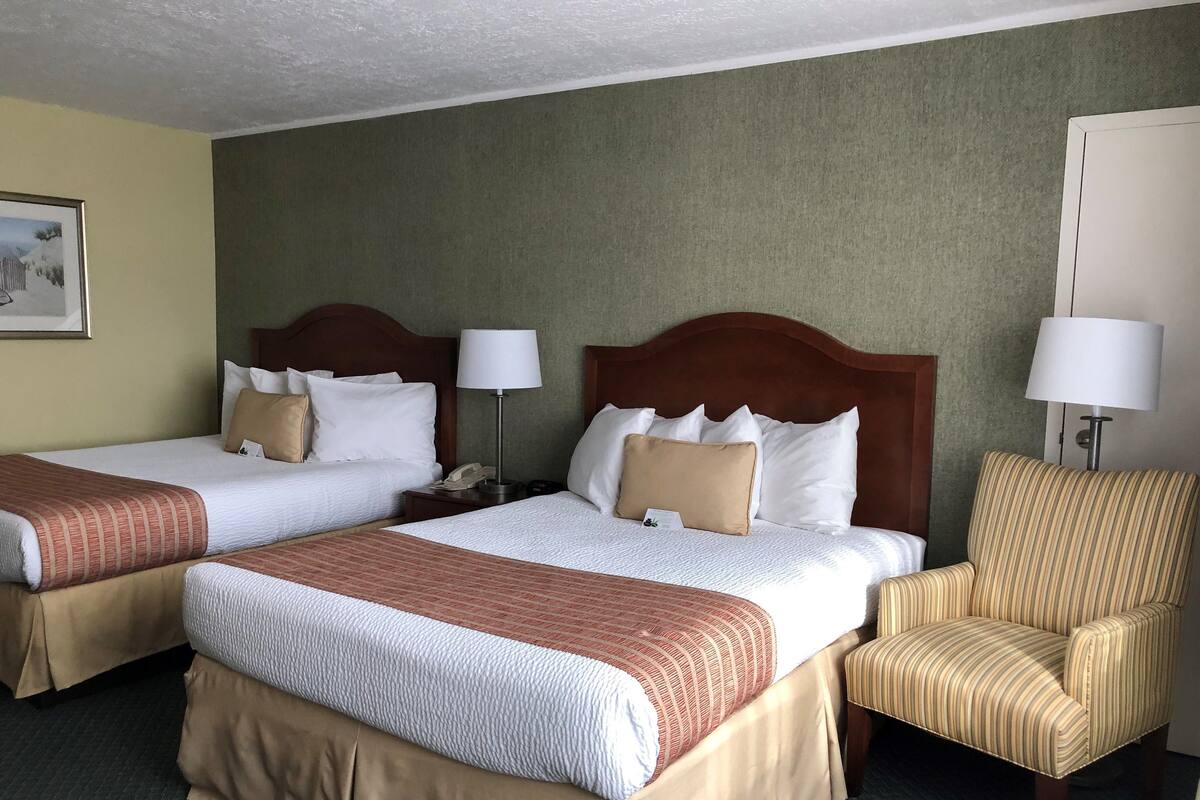 A hotel room with two beds, a chair, and a nightstand with a lamp.