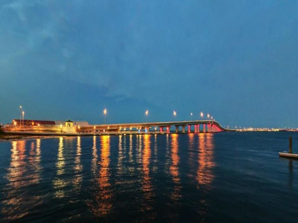 A long bridge with lights reflecting on the water at dusk.
