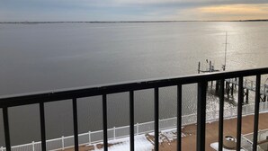 A view from a balcony overlooking a calm body of water with a distant shoreline, a wooden deck, and a white railing. - Pier 4 Hotel (Somers Point)