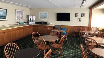 A hotel room with a kitchenette, a flat-screen TV, wooden chairs, and a patterned carpet.