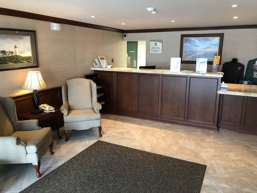 A hotel reception area with a reception desk, a chair, a lamp, and a framed picture on the wall.