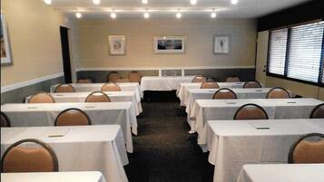 A conference room with rows of tables and chairs, framed pictures on the walls, and a window with blinds.