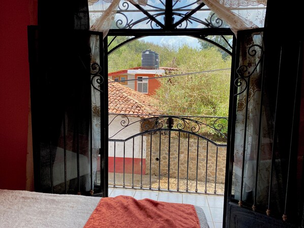 An open gate leading to a balcony with a tiled roof, a stone wall, and a view of a building with a red roof. - Hotel Real de la Sierra (Mazamitla)