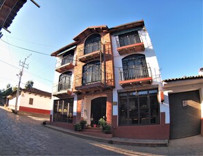 Un edificio de tres pisos con varios balcones, ventanas amplias y una calle adoquinada.