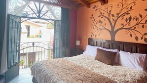 Een slaapkamer met een houten plafond, een bed met beddengoed met dessin, een muurschildering en een balkon met een ijzeren hek.