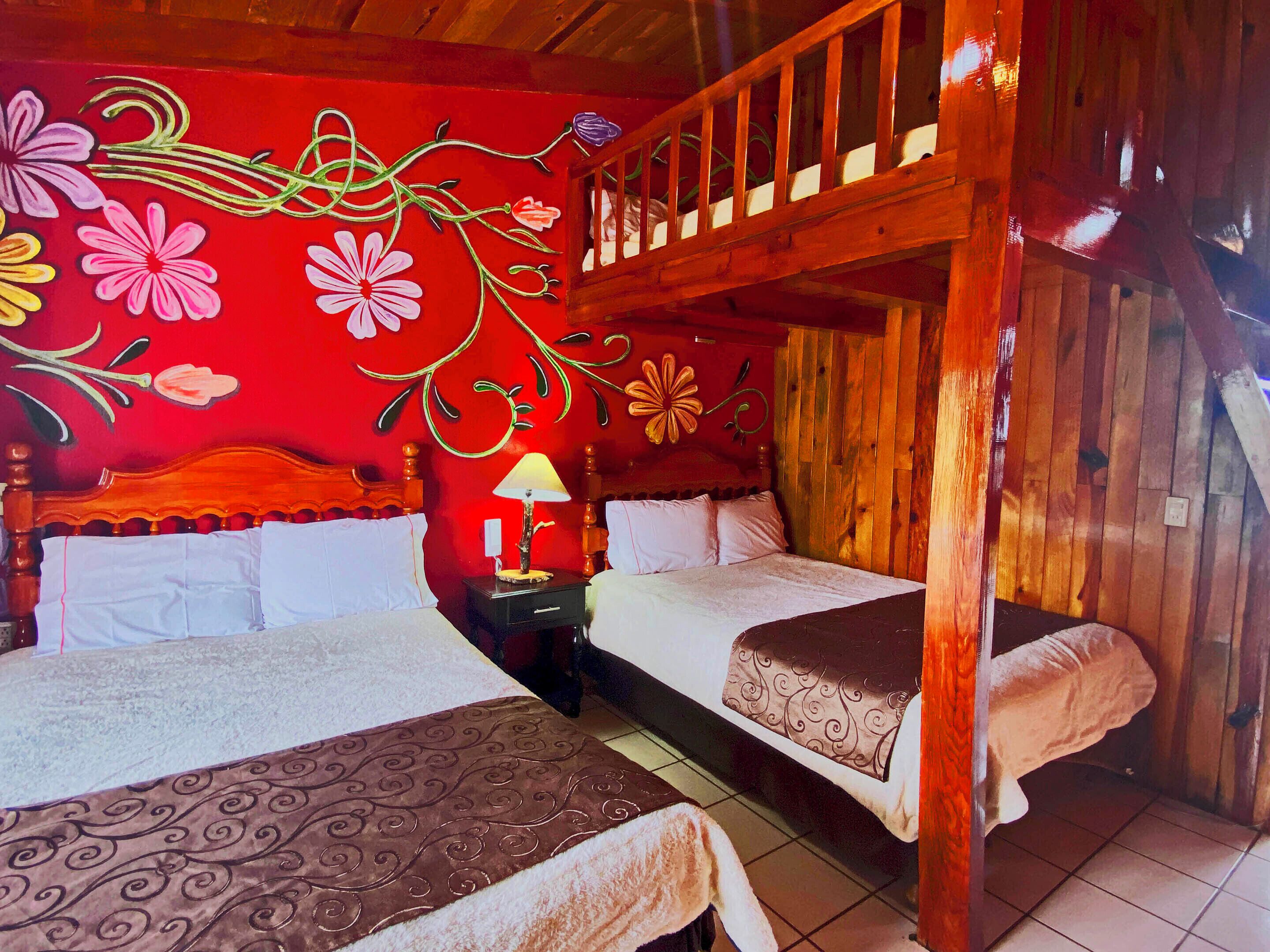 A room with two beds, wooden bunk beds, a red floral wall, and a wooden ceiling.
