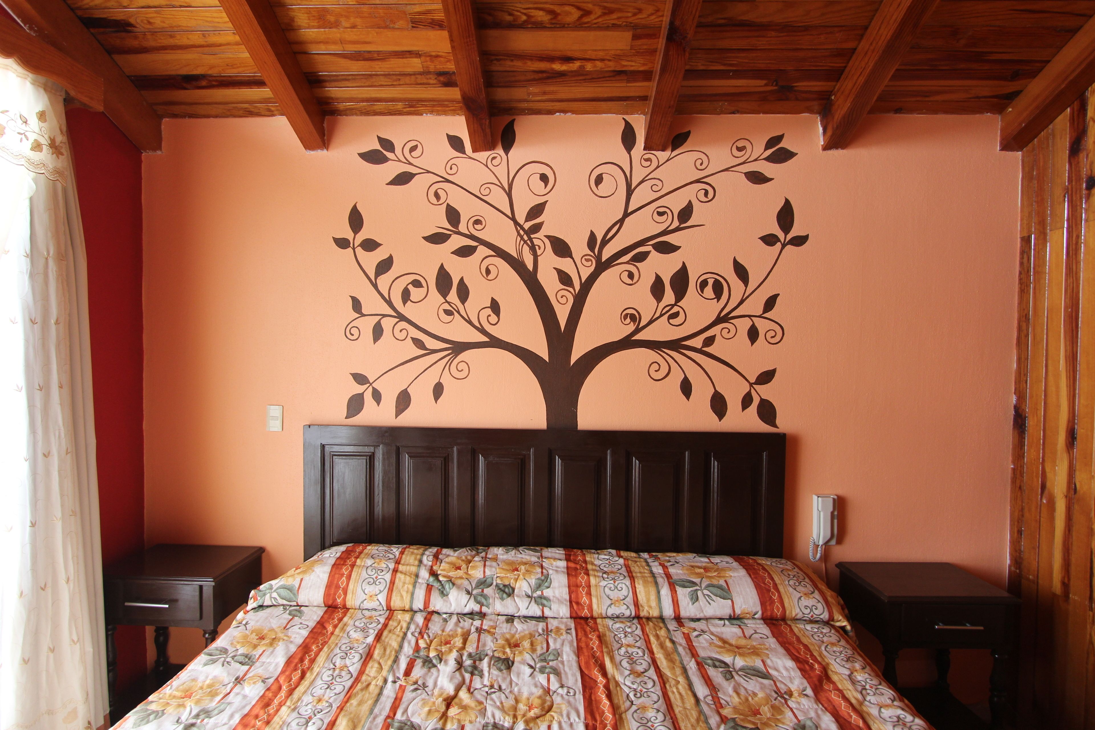 A bedroom with a bed, a nightstand, a wooden headboard, and a wall mural of a tree.