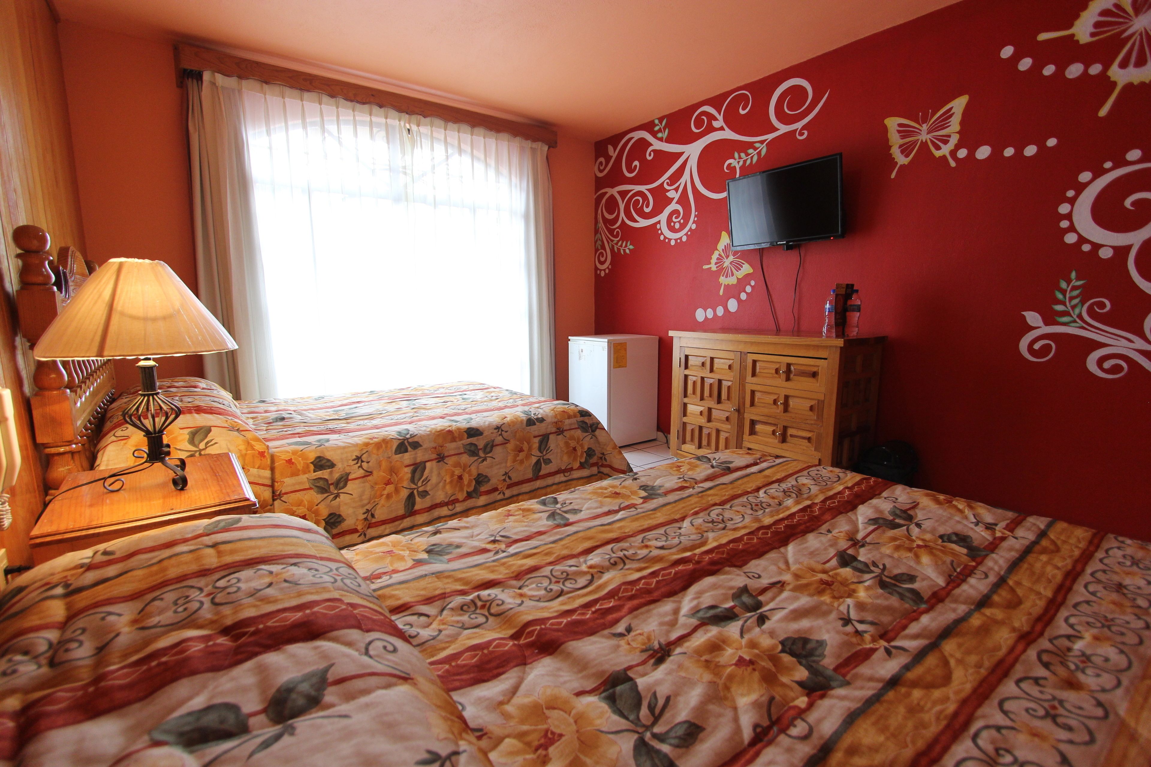 Een hotelkamer met twee bedden, een televisie, een houten dressoir en een raam met gordijnen.