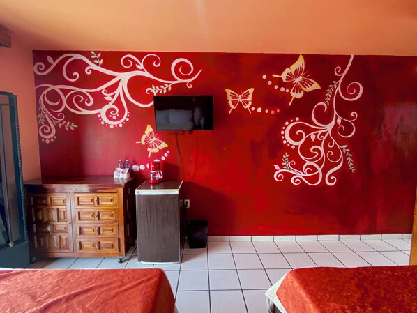 Habitación de hotel con pared roja, un armario de madera, una mesita con cafetera y dos camas.