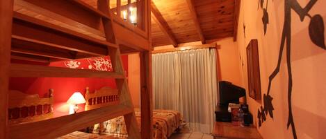 Una habitación acogedora con literas de madera, una mesita con una lámpara y una cama con edredón estampado de flores.