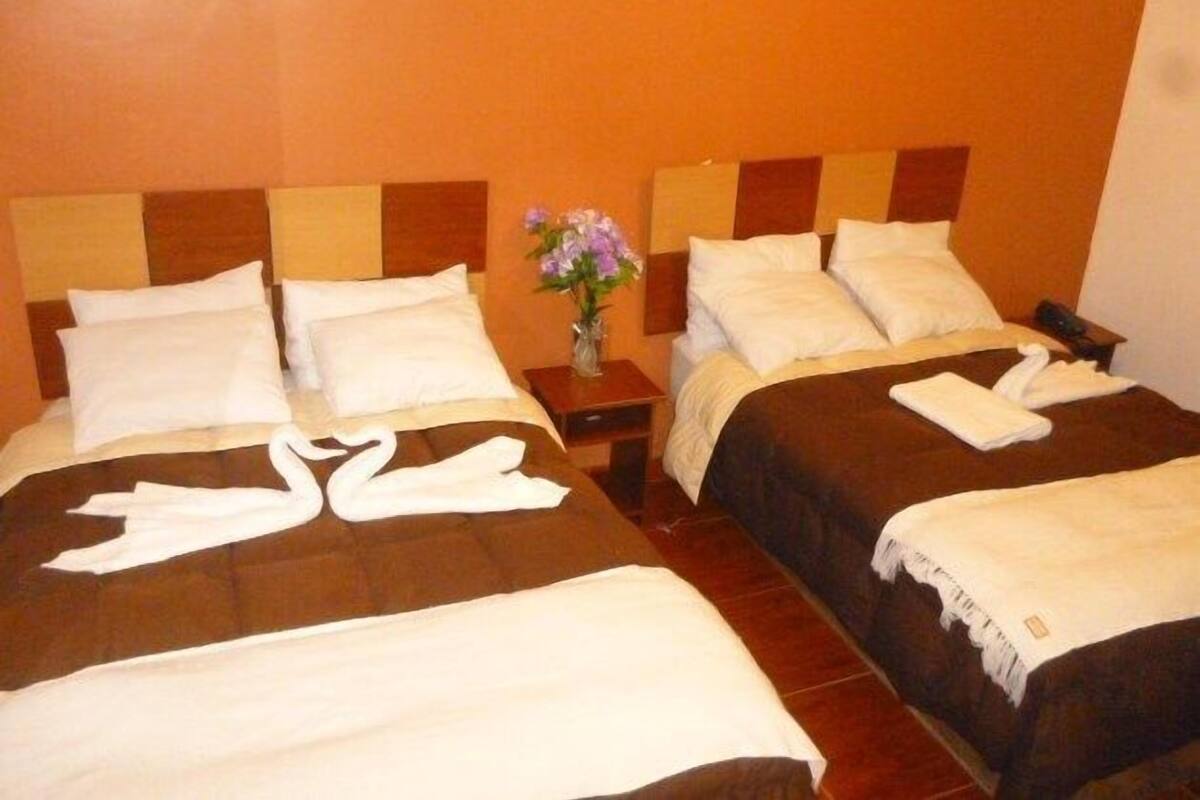 Une chambre d’hôtel avec deux lits, chacun doté de draps blancs et d’une tête de lit marron. Un vase rempli de fleurs violettes est posé sur une table de chevet entre les deux lits.