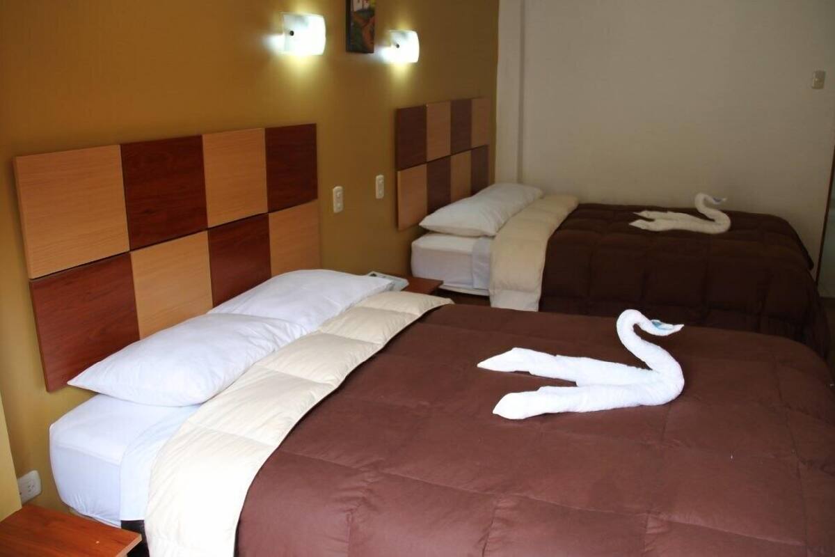 Une chambre d’hôtel avec un grand lit, un lit plus petit et deux serviettes en forme de cygne posées sur les lits.