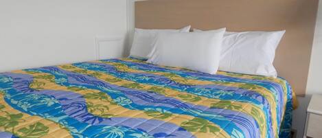 A hotel room with a bed featuring a colorful floral bedspread, white pillows, and a wooden headboard.