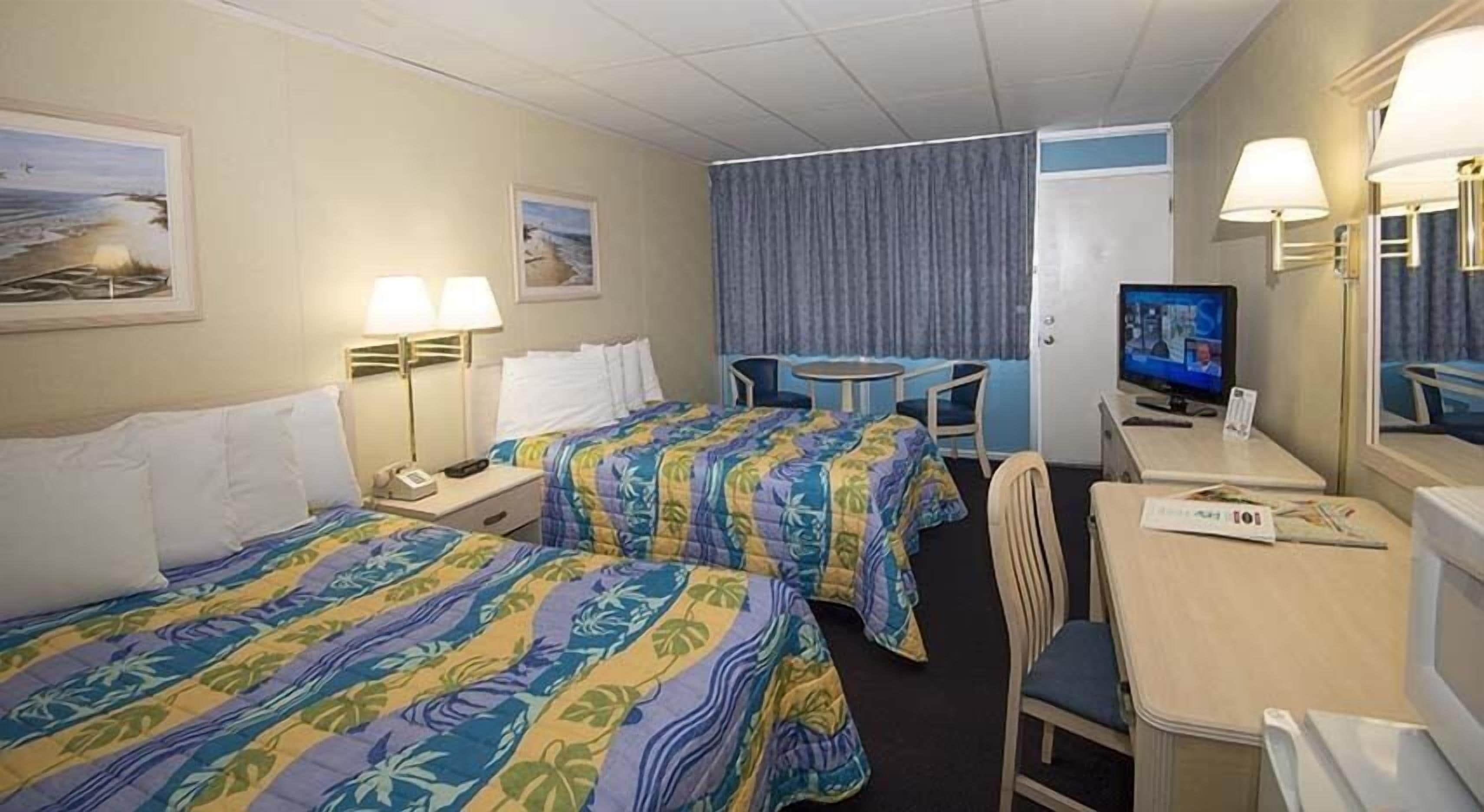 A hotel room with two beds, a desk, a chair, a television, and a window with curtains.
