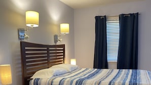 Een keurig opgemaakt slaapkamer met een houten bed, nachtlampjes, een nachtkastje en een raam met gordijnen.