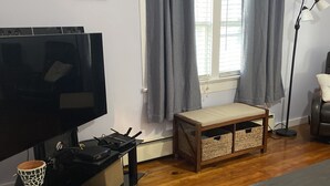 Een woonkamer met een flatscreen televisie, een bankje, een kleine tafel en een vloerlamp.