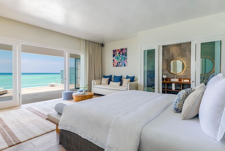 A hotel room with a large bed, a sofa, a round mirror, and a view of the ocean.