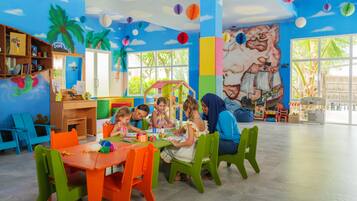 Una sala de juegos infantil llena de color, con un mural, ventanas amplias y muchos juguetes y actividades.