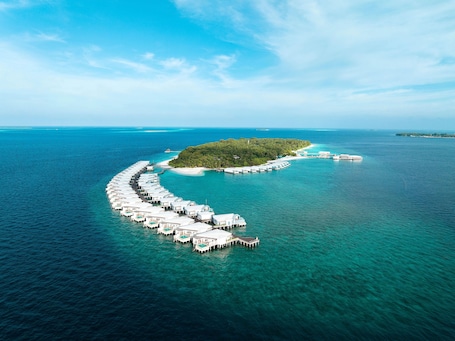 An aerial view of a resort island with overwater bungalows connected by a dock.