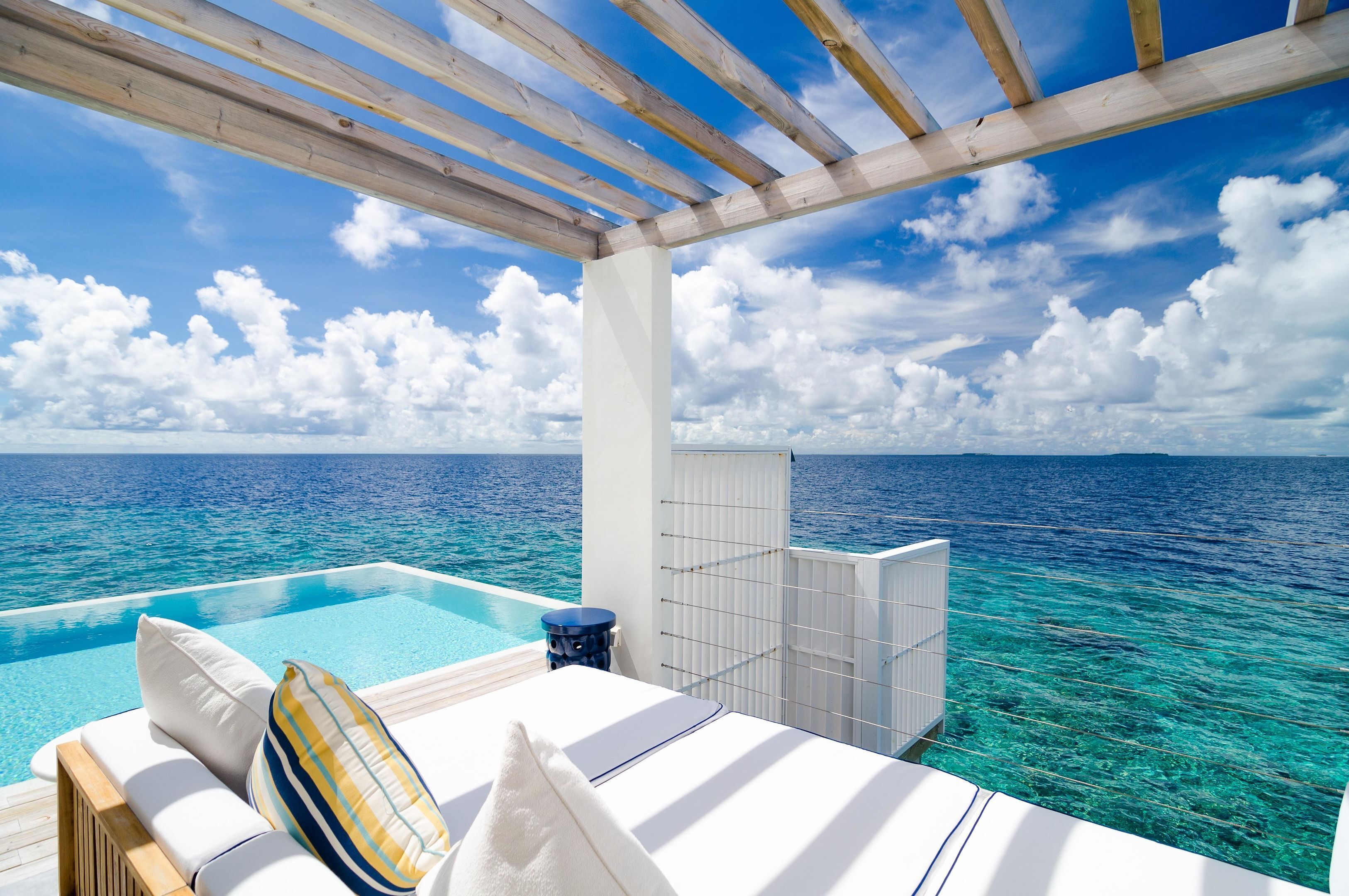 Un espace aménagé au bord de la piscine, avec vue sur l’océan, une pergola en bois et une structure recouverte de carreaux blancs.