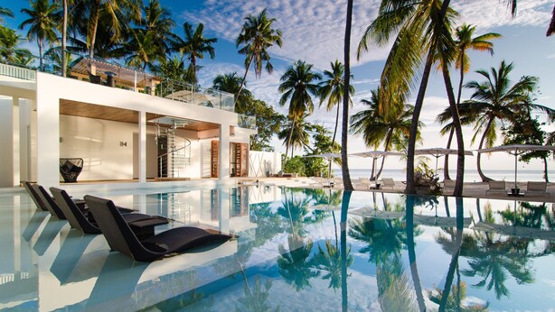 A modern pool area with lounge chairs, a glass-enclosed structure, and palm trees. - Amilla Maldives (Finolhas Island)