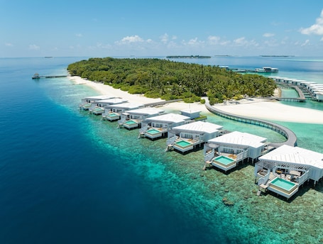 An aerial view of overwater bungalows with clear blue waters and a sandy beach.