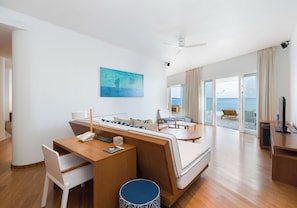 A modern hotel room with a wooden desk, a sofa, a television, and a large window offering a view of the sea. - Amilla Maldives (Finolhas Island)