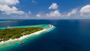 An aerial view of a tropical island with a long stretch of overwater bungalows, clear turquoise waters, and lush greenery.