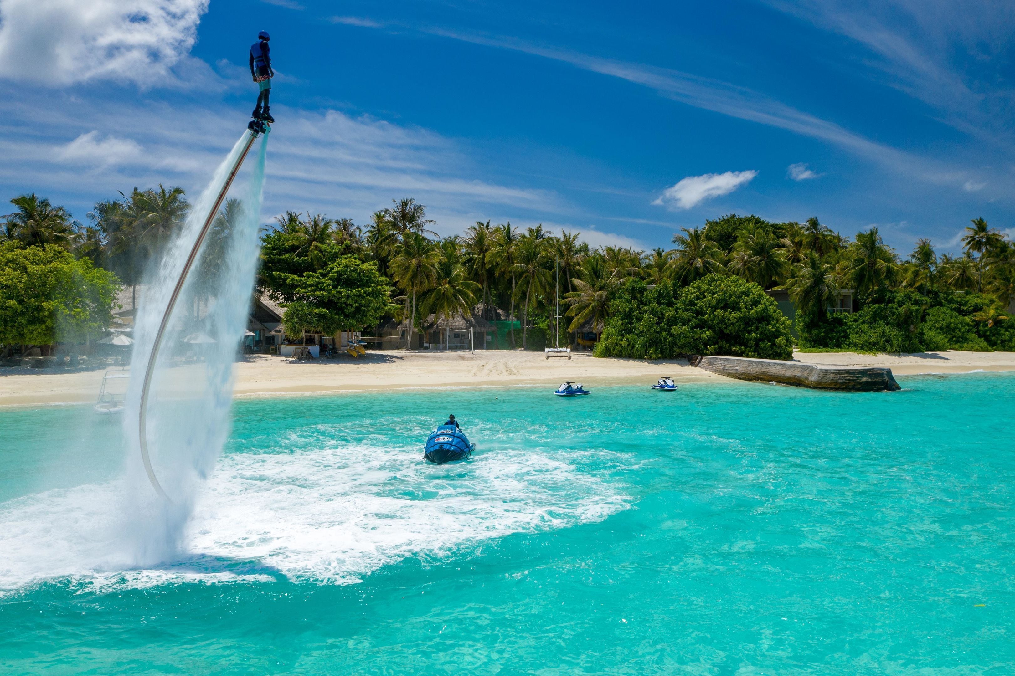 A water jet ride at a beachside resort with clear turquoise water, palm trees, and a sandy beach.
