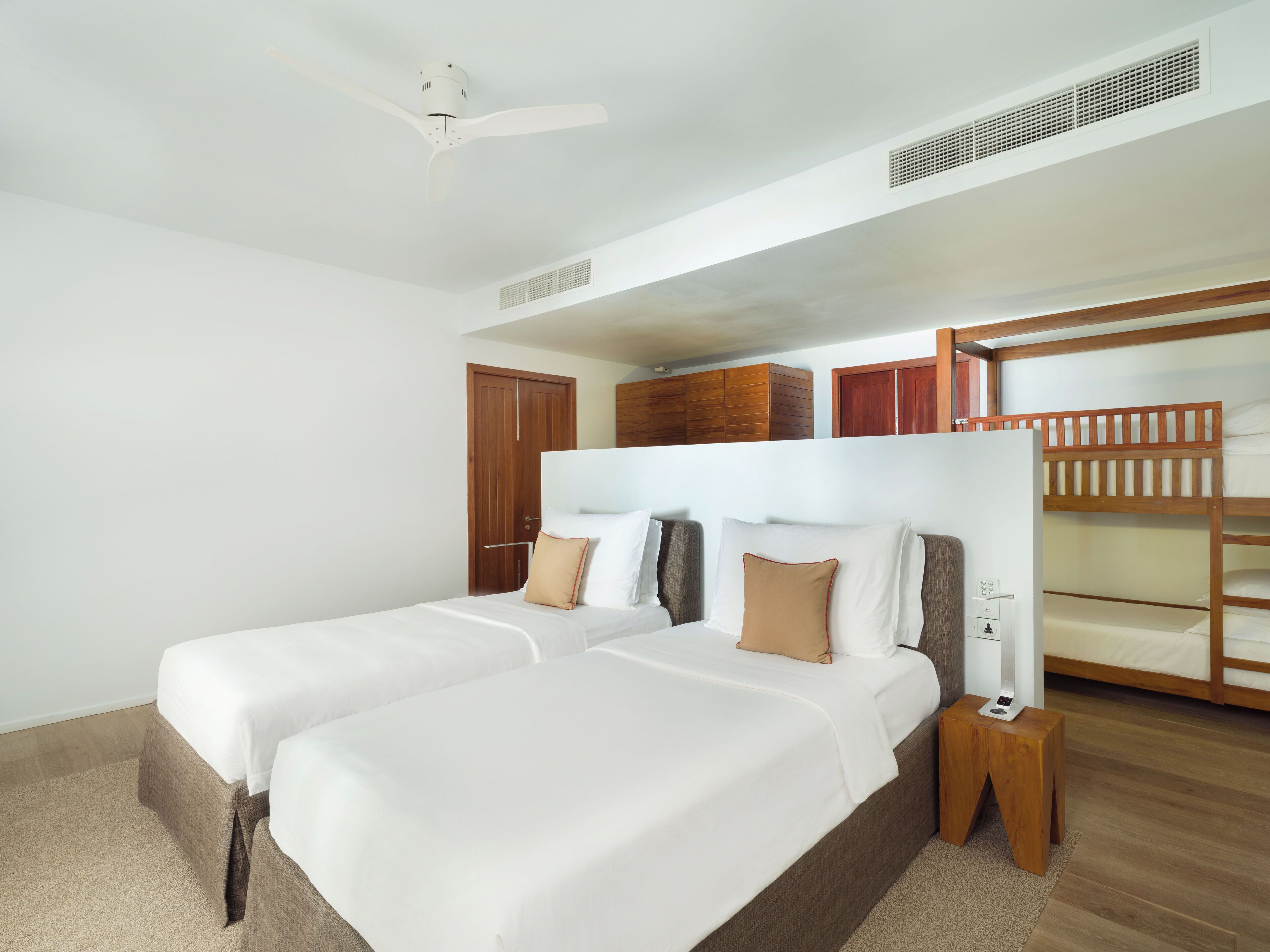 Een hotelkamer met twee bedden, een plafondventilator, houten stapelbedden en een klein nachtkastje.