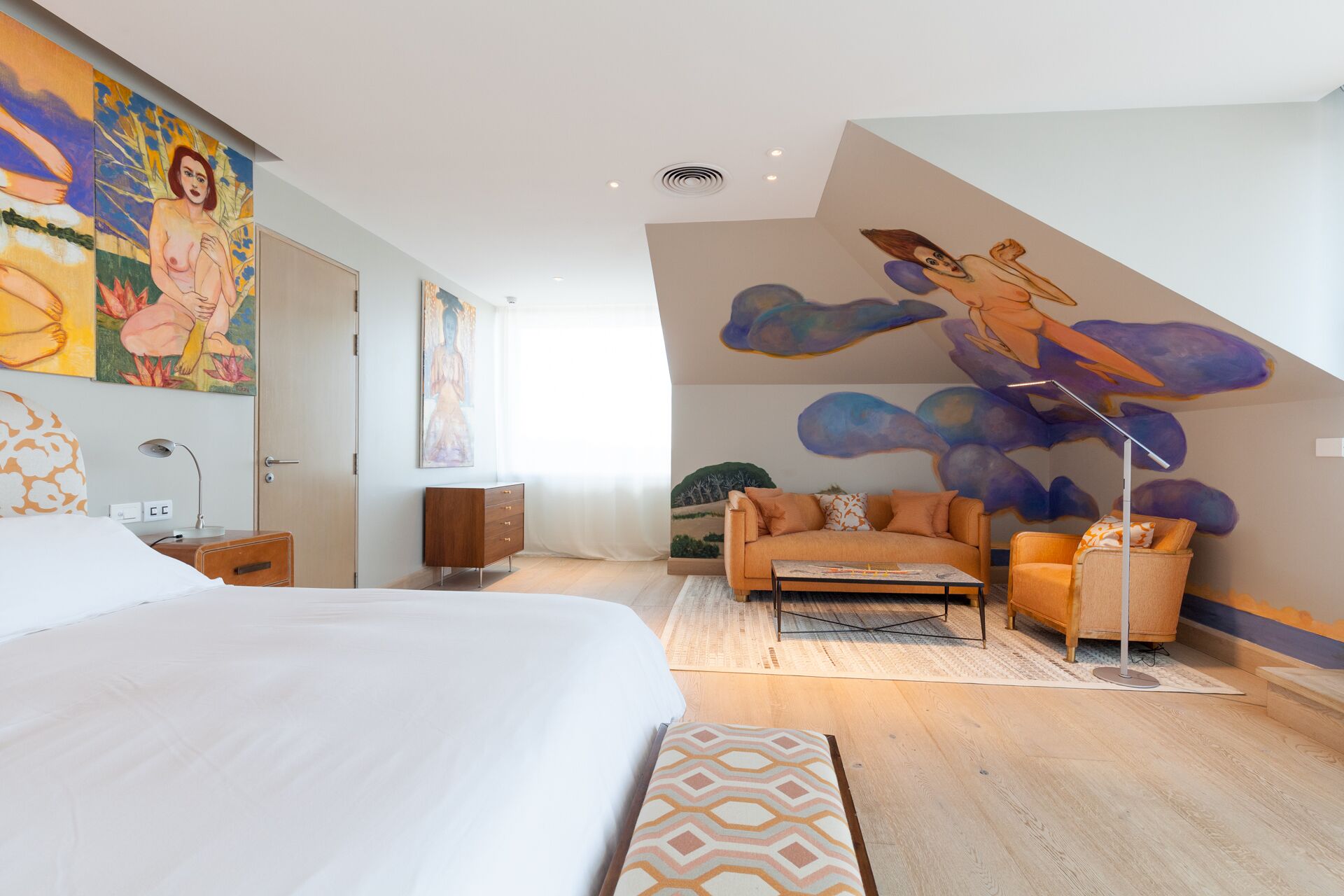 Una habitación de hotel moderna con una cama grande, un sofá, una mesa de centro y un mural en la pared.