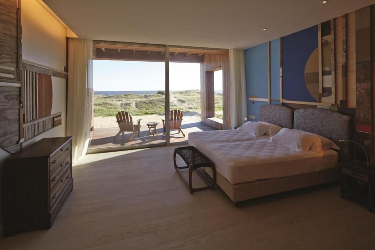 A bedroom with a large bed, a dresser, and a view of the beach through a sliding door.