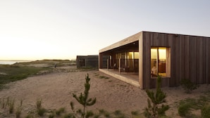 A modern beach house with large windows, a wooden exterior, and a sandy beach in the background. - Bahia Vik Jose Ignacio (José Ignacio)