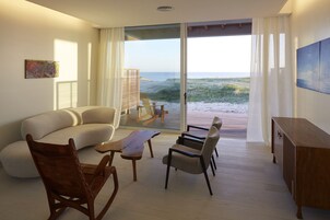 Un soggiorno moderno con un divano curvo, sedie in legno, un tavolino da caffè e vista sulla spiaggia tramite ampie vetrate.