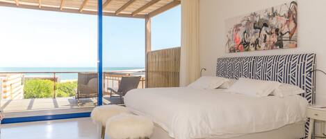 A bedroom with a large bed, a view of the sea, and a balcony with a chair.