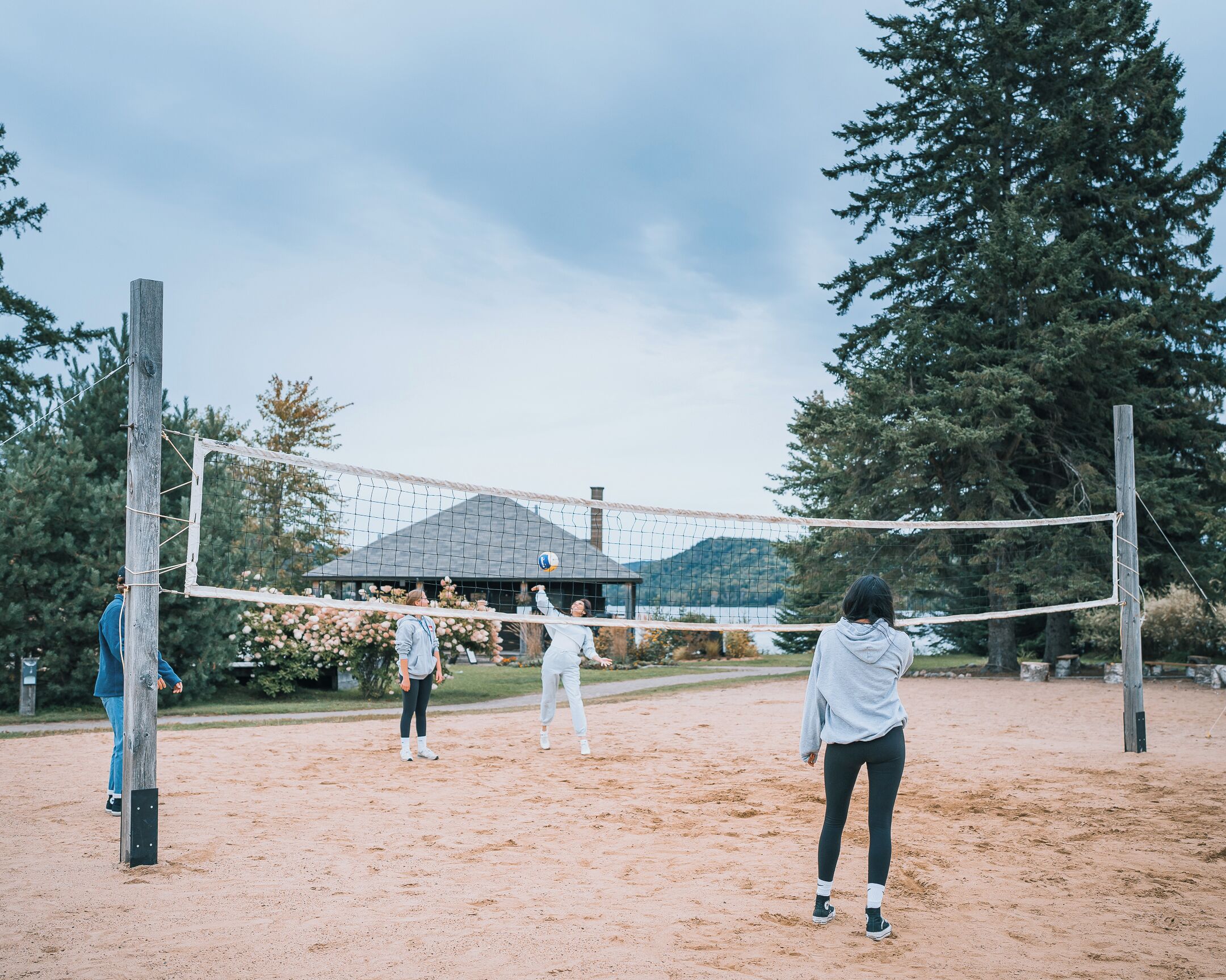 A volleyball court with a net, surrounded by trees and a building in the background.